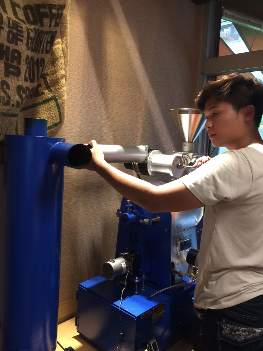 博任站在外觀藍色、幾乎和博任一樣高的烘豆機前，咖啡師的氣勢已顯露無遺